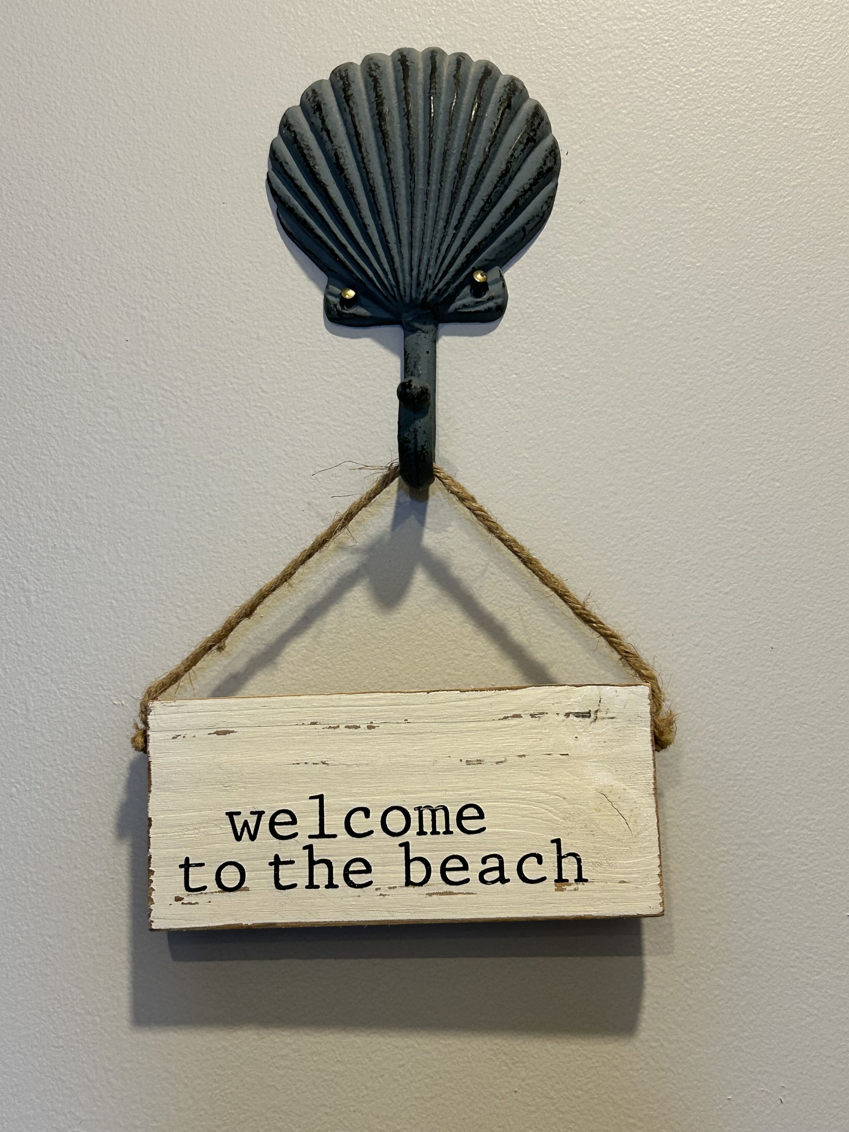 Une pancarte en bois portant l’inscription « Bienvenue à la plage » est accrochée à un mur.