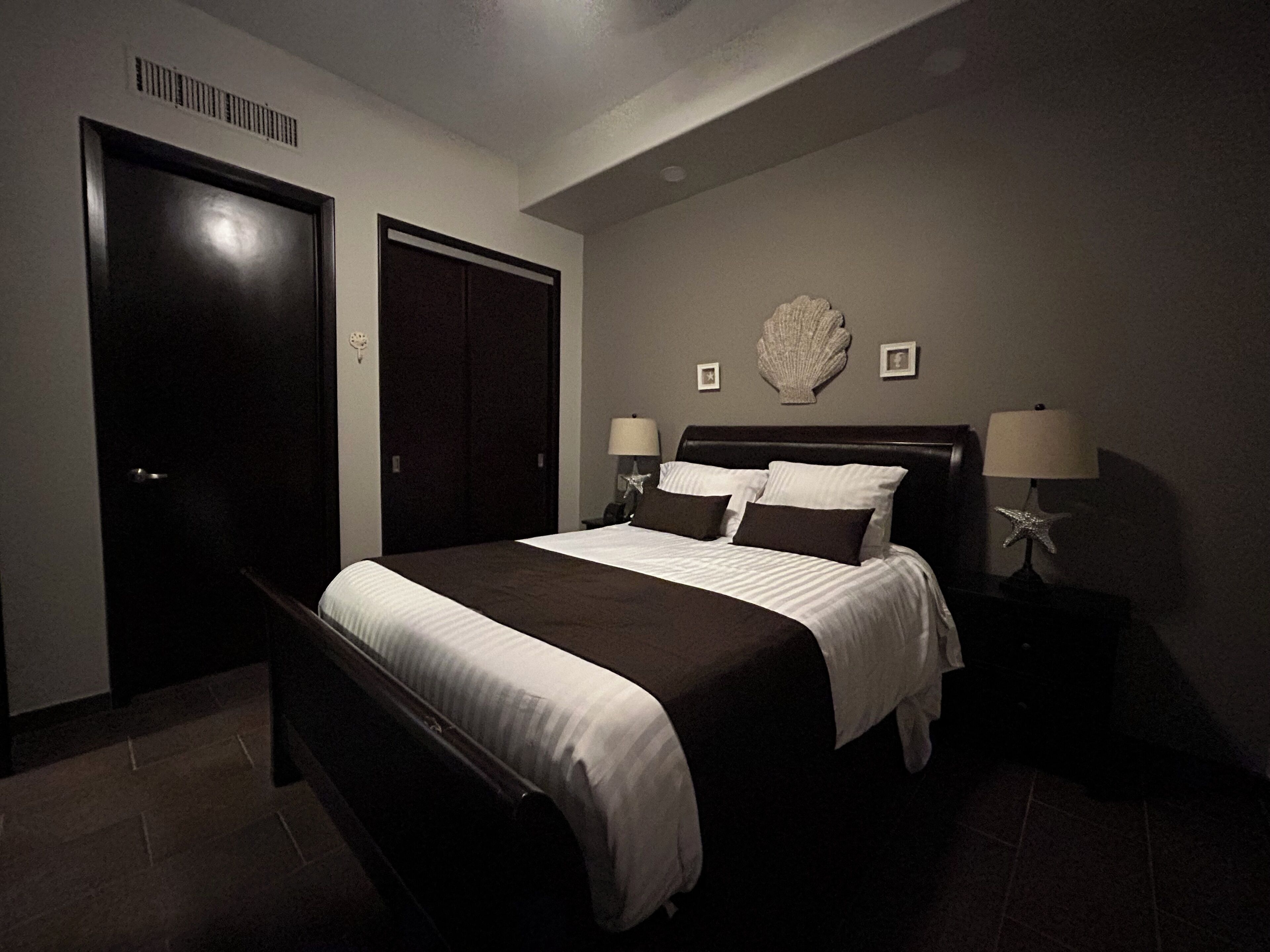 Une chambre à coucher avec un grand lit, une armoire en bois foncé et une table de chevet sur laquelle se trouvent une lampe et un coquillage décoratif.