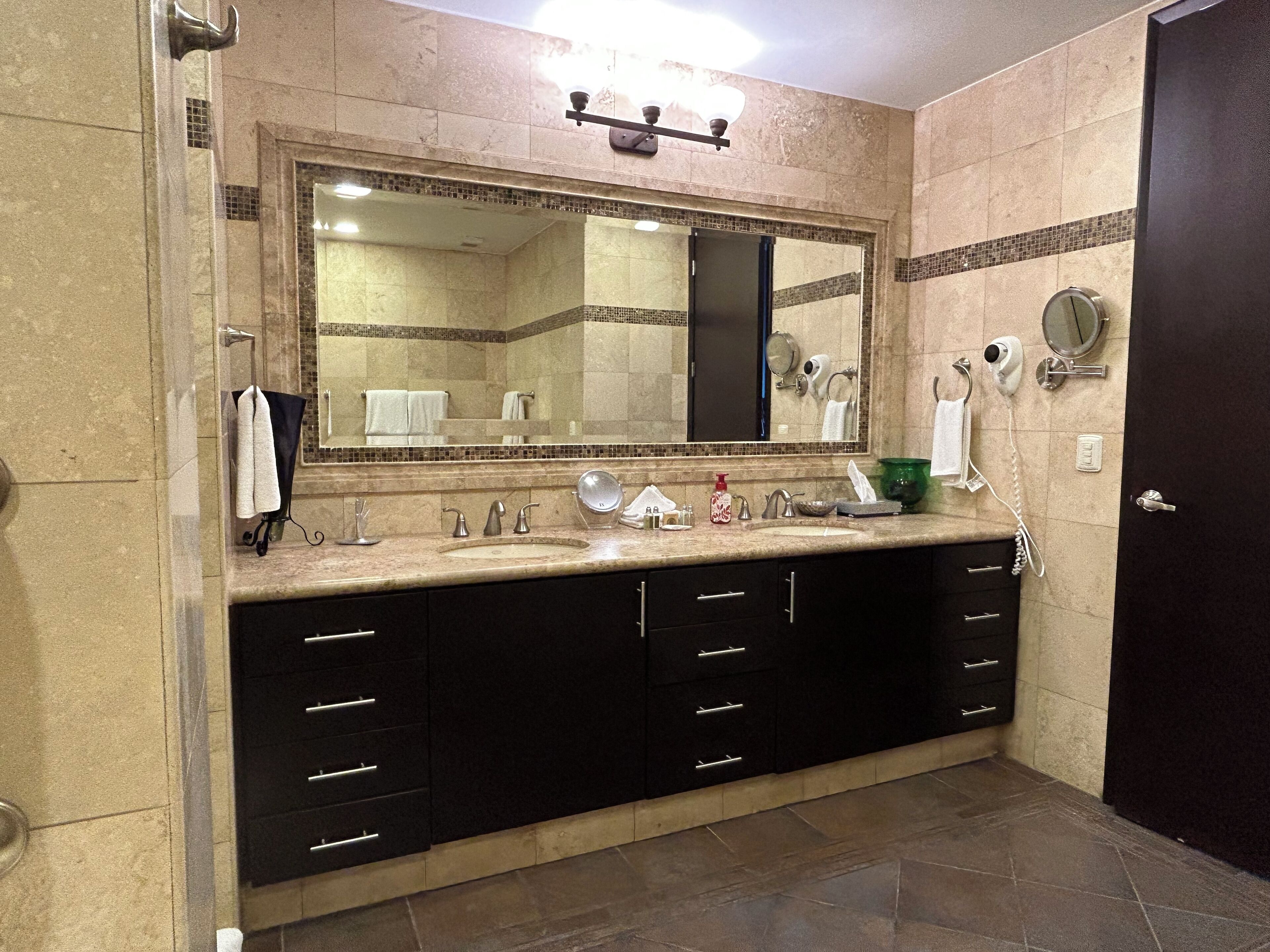 Un baño con un espejo grande, un lavabo, un mueble de tocador con cajones y un secador de pelo en la pared.