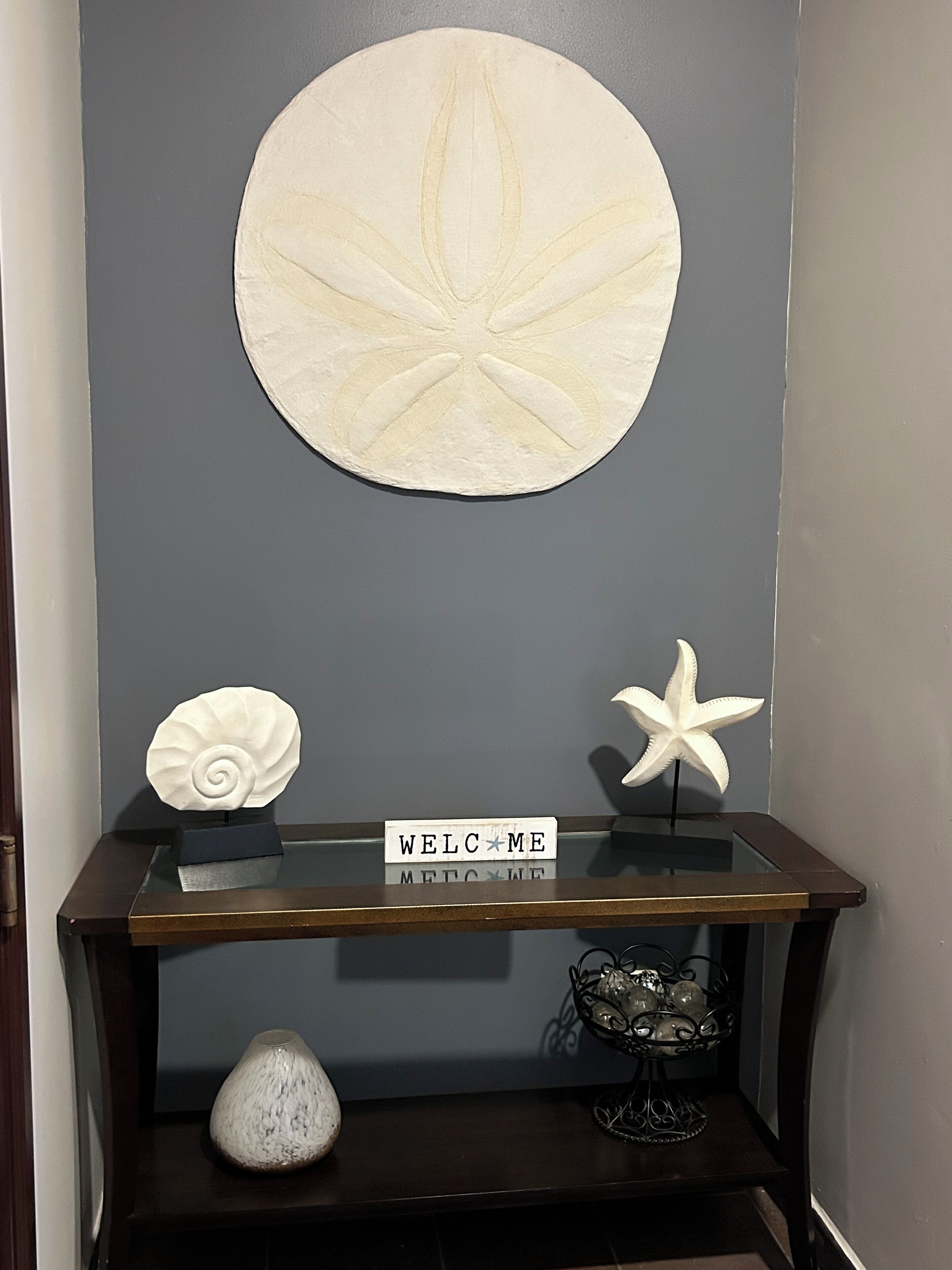 A display table with a welcome sign, a seashell, a starfish, and a vase.