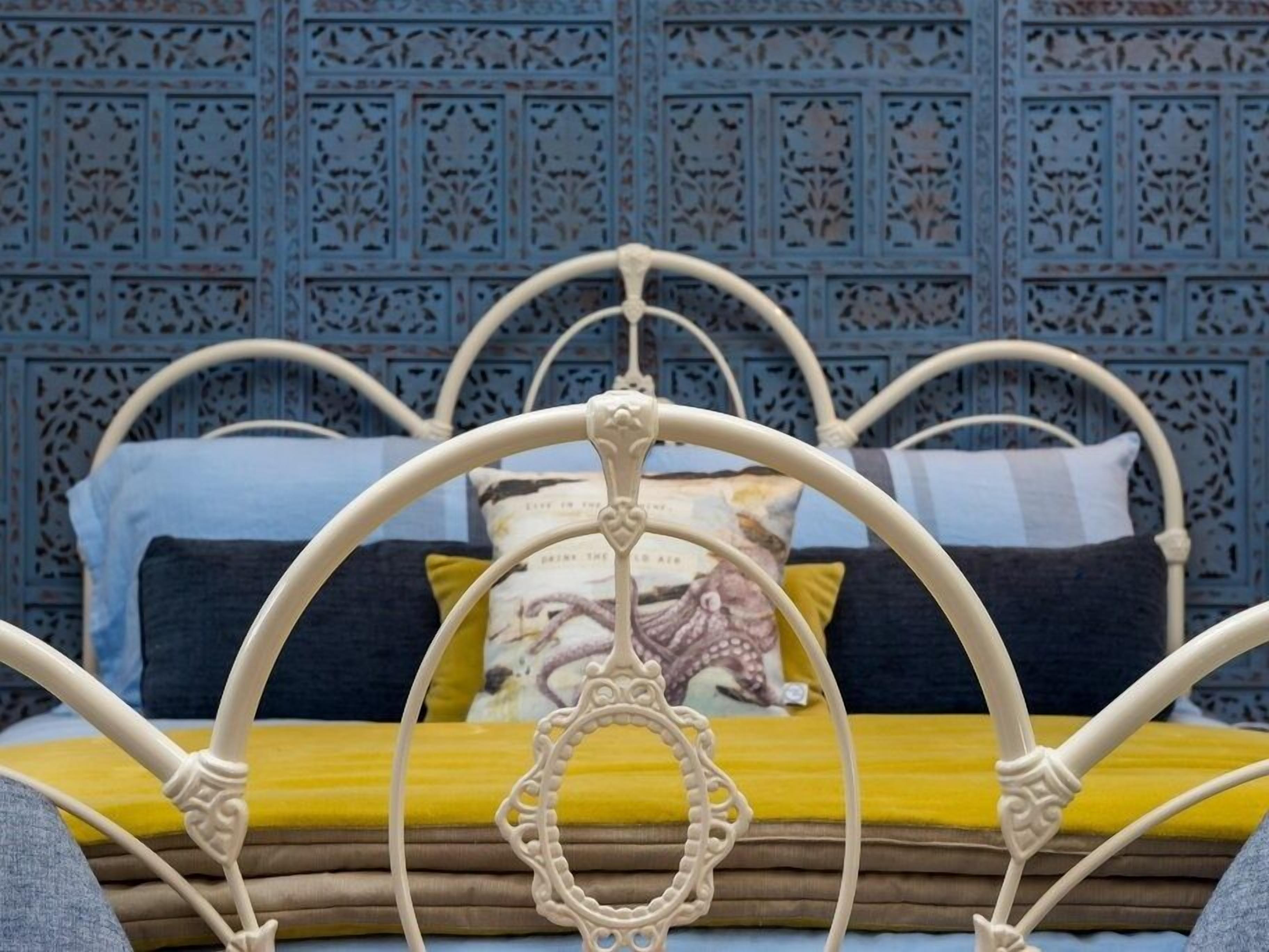 A bed with a white metal frame, multiple pillows, and a patterned wall in the background.