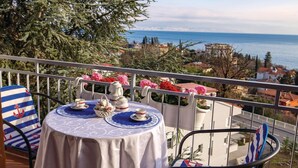 A balcony with a table set for tea, overlooking a coastal cityscape.
