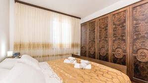 A hotel room with a large bed, a wooden wardrobe, and a window with sheer curtains.