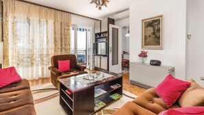 A living room with a sofa, armchair, and coffee table. There is a dining area with a table and chairs. A painting is on the wall.