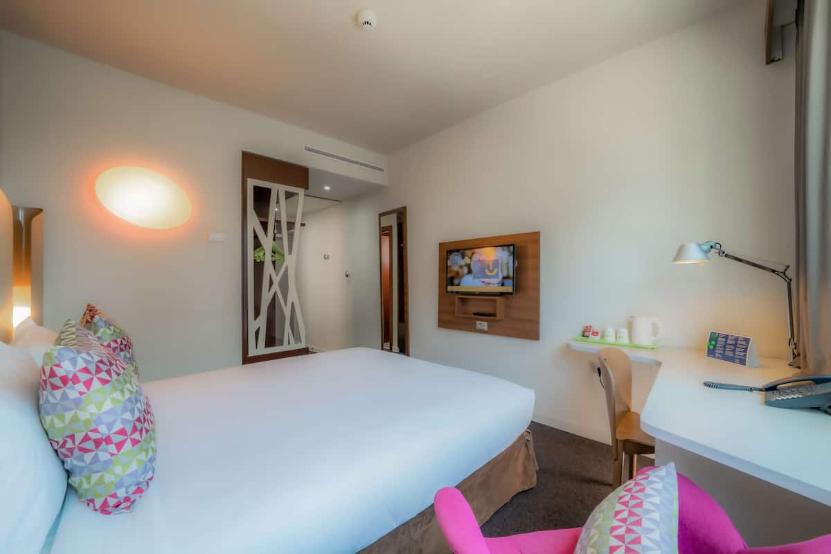A hotel room with a bed, a desk with a chair, a television, and a lamp.