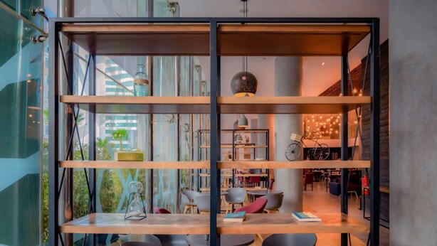 A modern interior with a wooden shelving unit, tables, and chairs. - Hotel Campanile Casablanca Centre Ville (Casablanca)