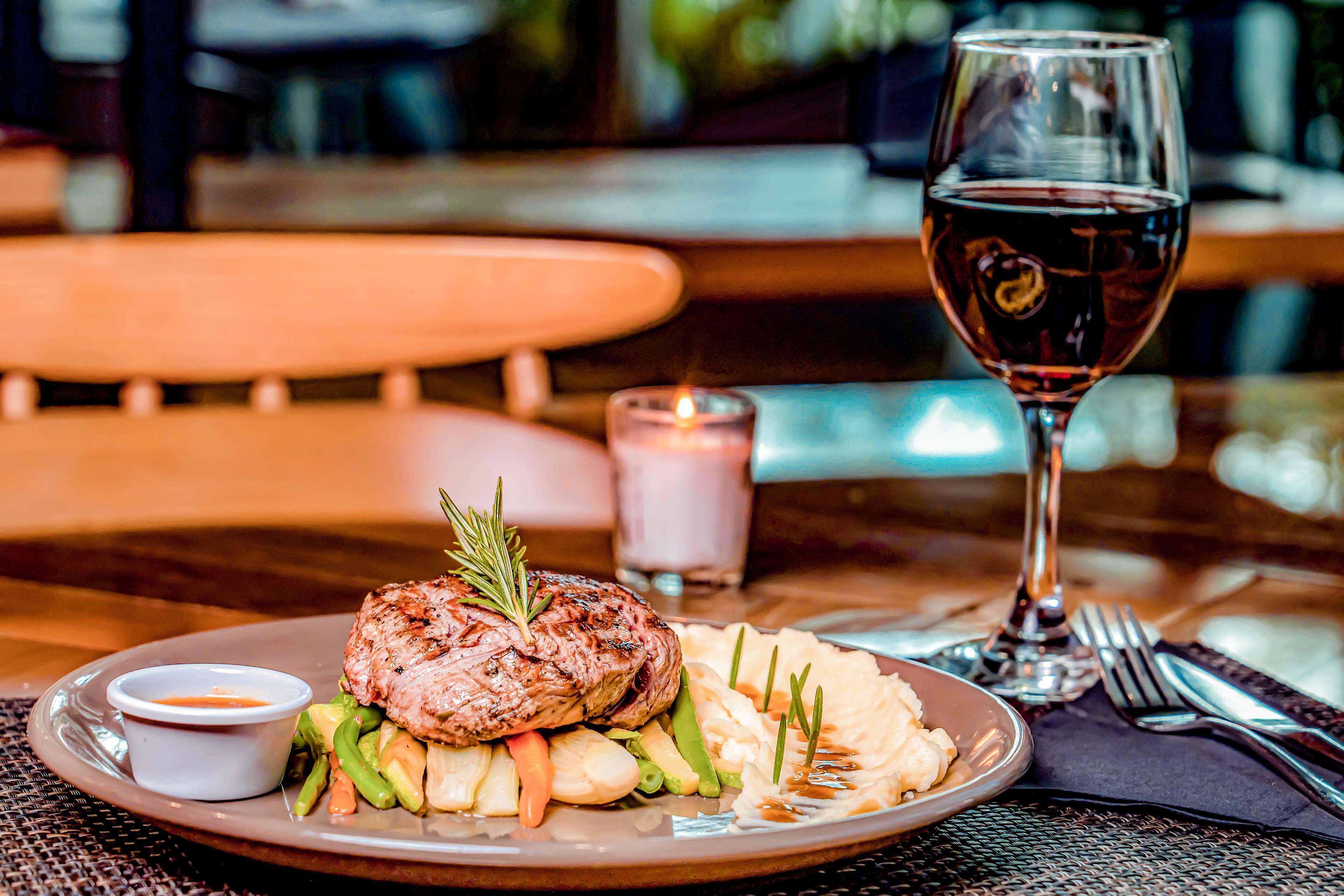 A plate of food with a steak, vegetables, and a glass of red wine on a table.