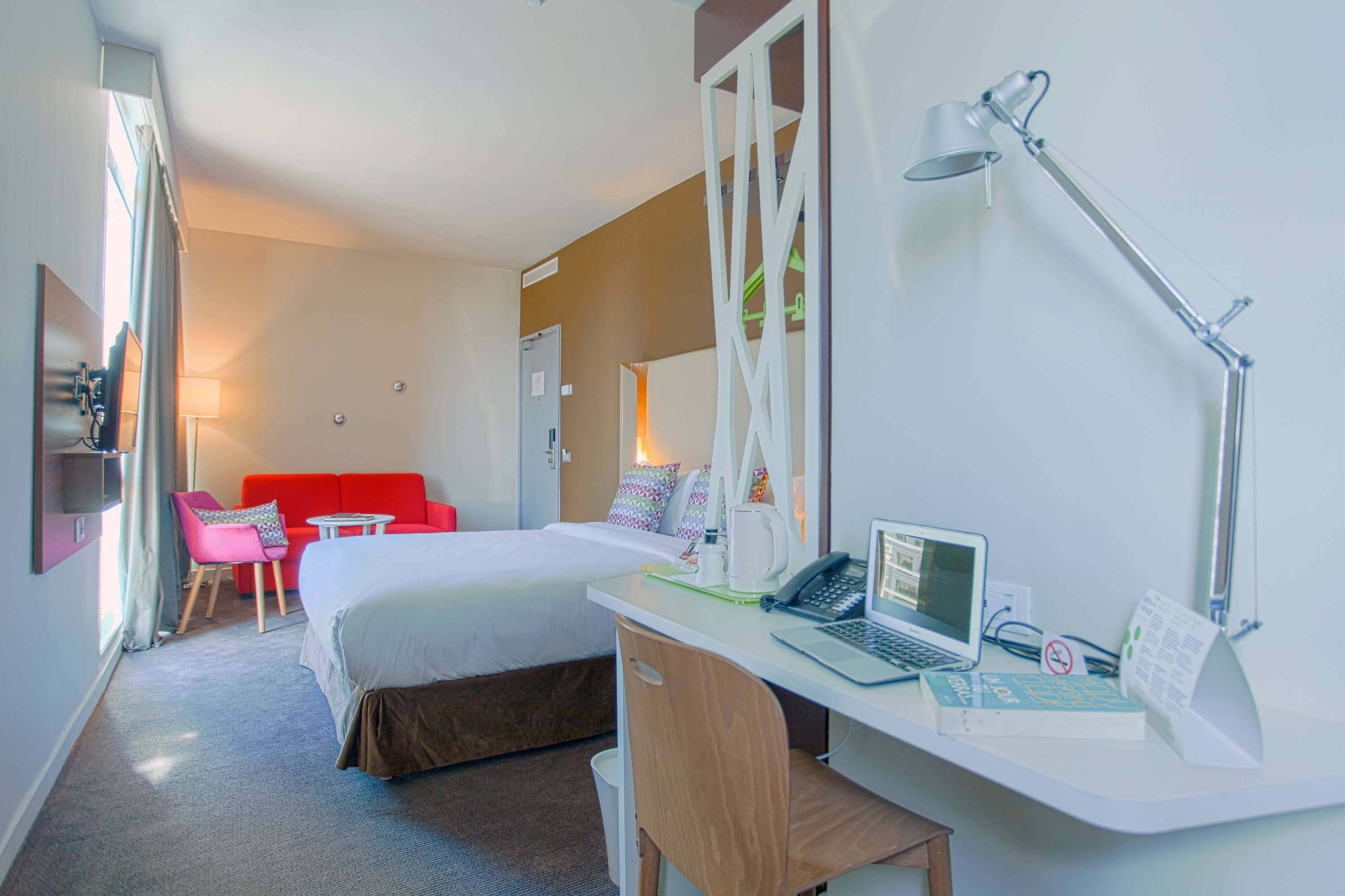 Ein Hotelzimmer mit Bett, Schreibtisch, Laptop und einer roten Couch.