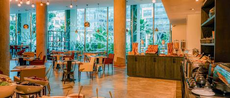 Un restaurante espacioso con techos altos, lámparas colgantes y amplios ventanales que ofrecen vista a plantas de interior.
