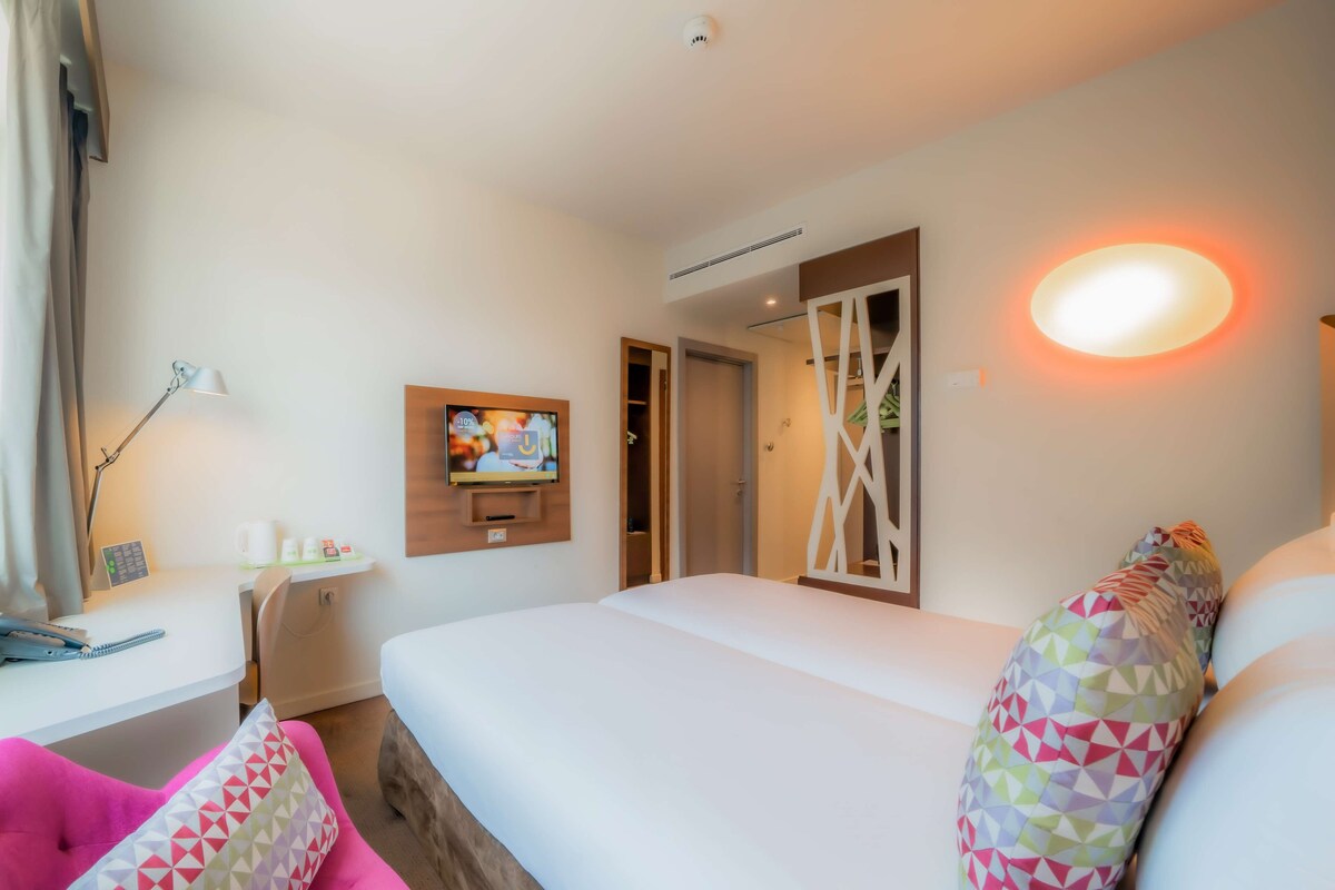 Habitación de hotel con cama, escritorio, silla, televisor y puerta del baño.