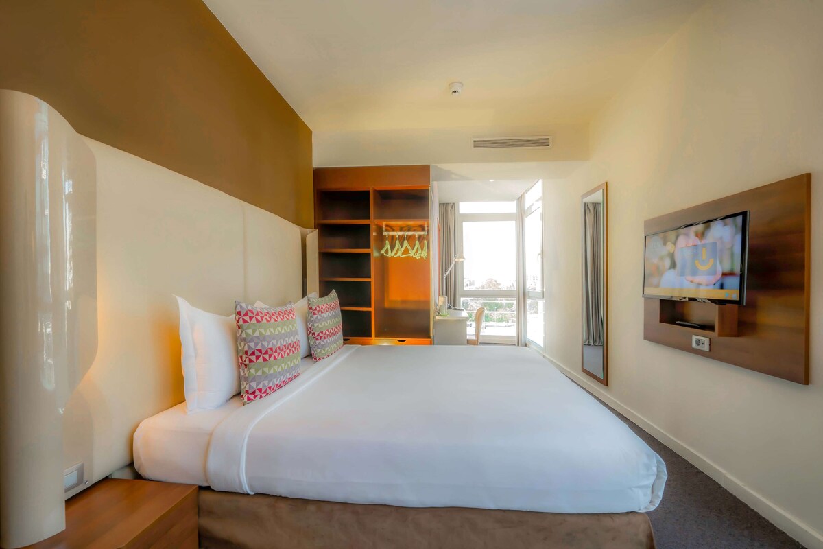 Habitación de hotel con una cama grande, televisión montada en la pared, armario y balcón con vistas.