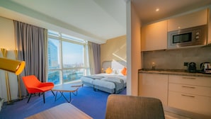 A hotel room with a bed, a desk, a chair, a kitchenette, and a large window with curtains. - Hotel Campanile Casablanca Centre Ville (Casablanca)