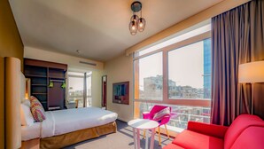 A modern hotel room with a bed, a red sofa, a small table, and a large window offering a city view. - Hotel Campanile Casablanca Centre Ville (Casablanca)
