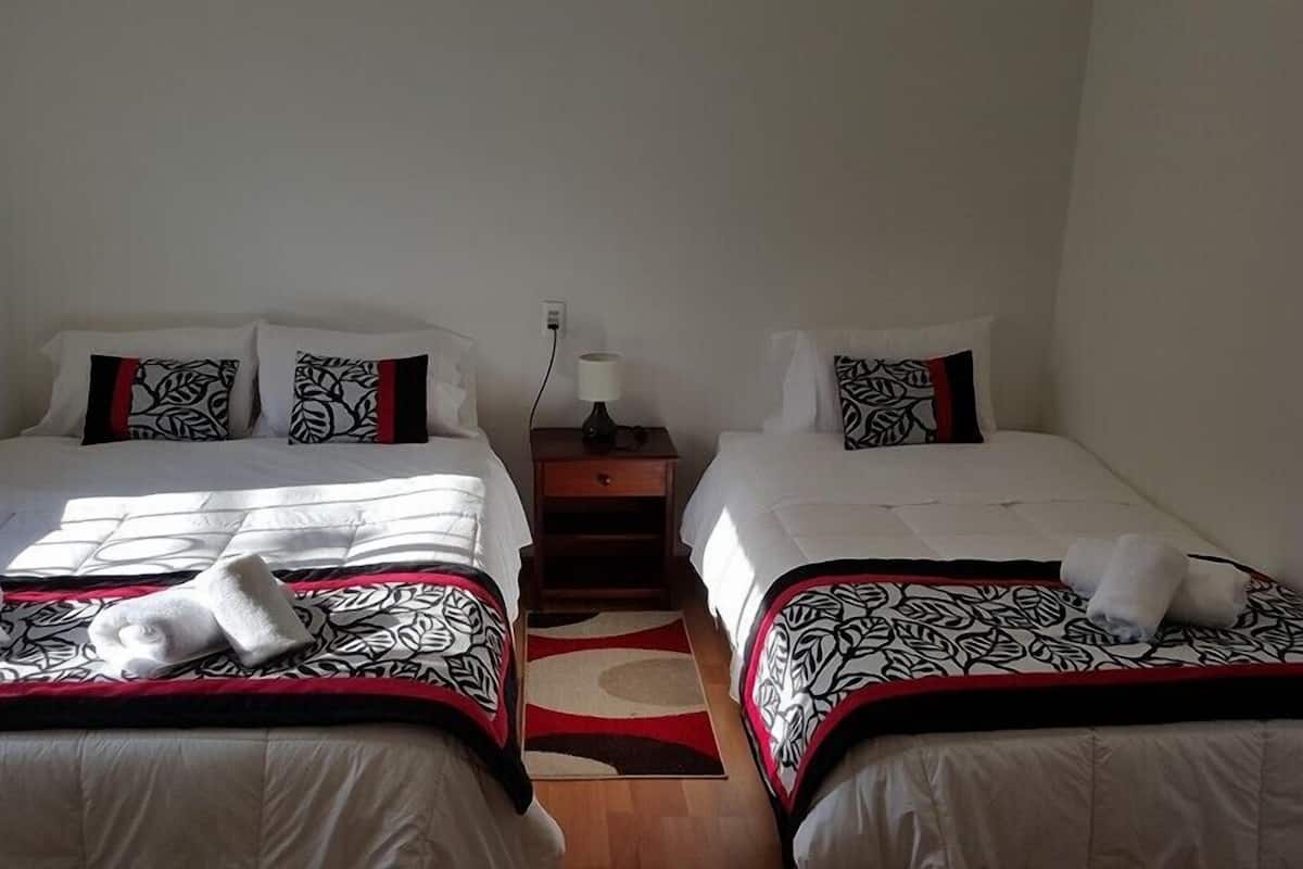 Dos camas individuales con ropa de cama y toallas estampadas, una mesita de noche con lámpara, y suelo de madera.