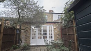 A courtyard with a brick wall, a white door, and a green metal table and chairs. - Traditional Home in Kew Gardens (Richmond)