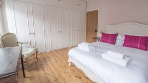 A bedroom with a wooden floor, a bed with white bedding and pink pillows, a chair, and a wardrobe. - Traditional Home in Kew Gardens (Richmond)