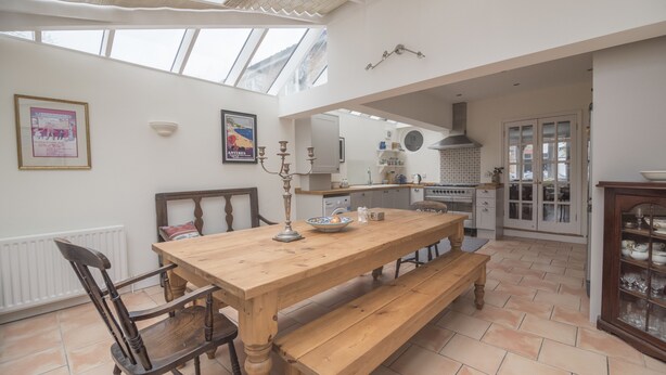 A spacious kitchen with a wooden table, bench, and a large window above the counter. - Traditional Home in Kew Gardens (Richmond)