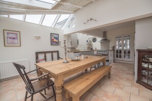 Een ruime keuken met een houten tafel, een bankje en een groot raam boven de aanrecht.