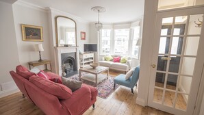 A living room with a red sofa, a white sofa, a blue armchair, a fireplace, and a large window with a view of the city. - Traditional Home in Kew Gardens (Richmond)