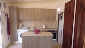 A compact kitchen with wooden cabinets, a washing machine, a microwave, and a refrigerator. -  exceptional holidays  (Gouvès Hersonissos Crête Grèce)