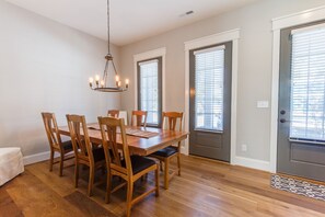 Une salle à manger avec une table et des chaises en bois, un lustre et une porte avec une fenêtre.