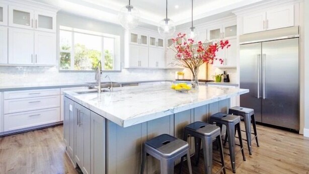 A modern kitchen with a large island, white cabinetry, stainless steel appliances, and bar stools.