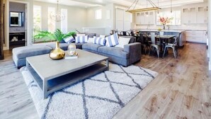 A modern living room with a sectional sofa, a coffee table, and a dining area with a chandelier.