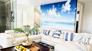 A living room with a white sectional sofa, a coffee table with a bowl of lemons, a decorative vase, and a large painting of a beach scene.