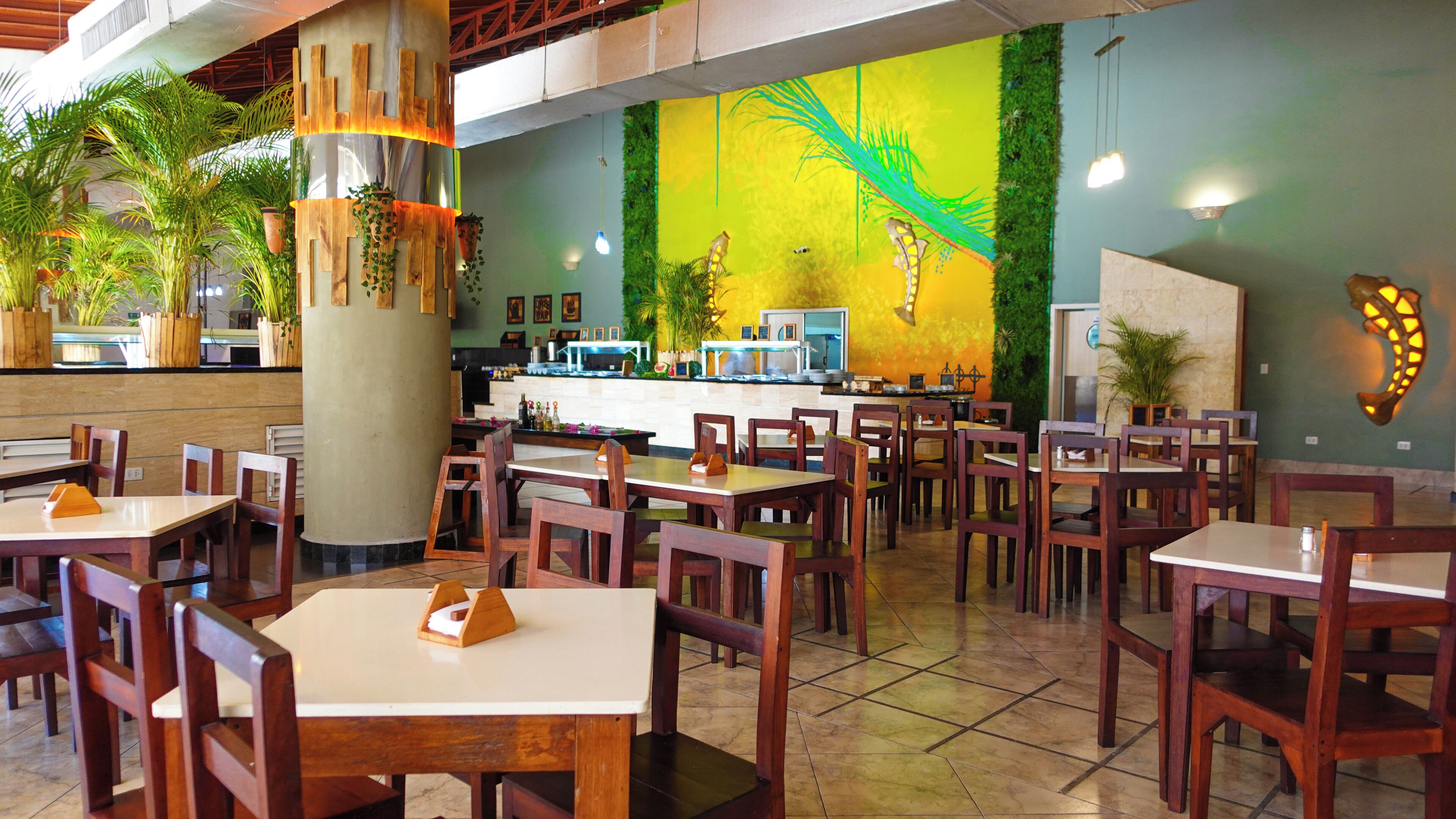 A restaurant with wooden tables and chairs, a counter with a display of bottles, and a mural on the wall.