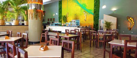 A restaurant with wooden tables and chairs, a counter with a display of bottles, and a mural on the wall.