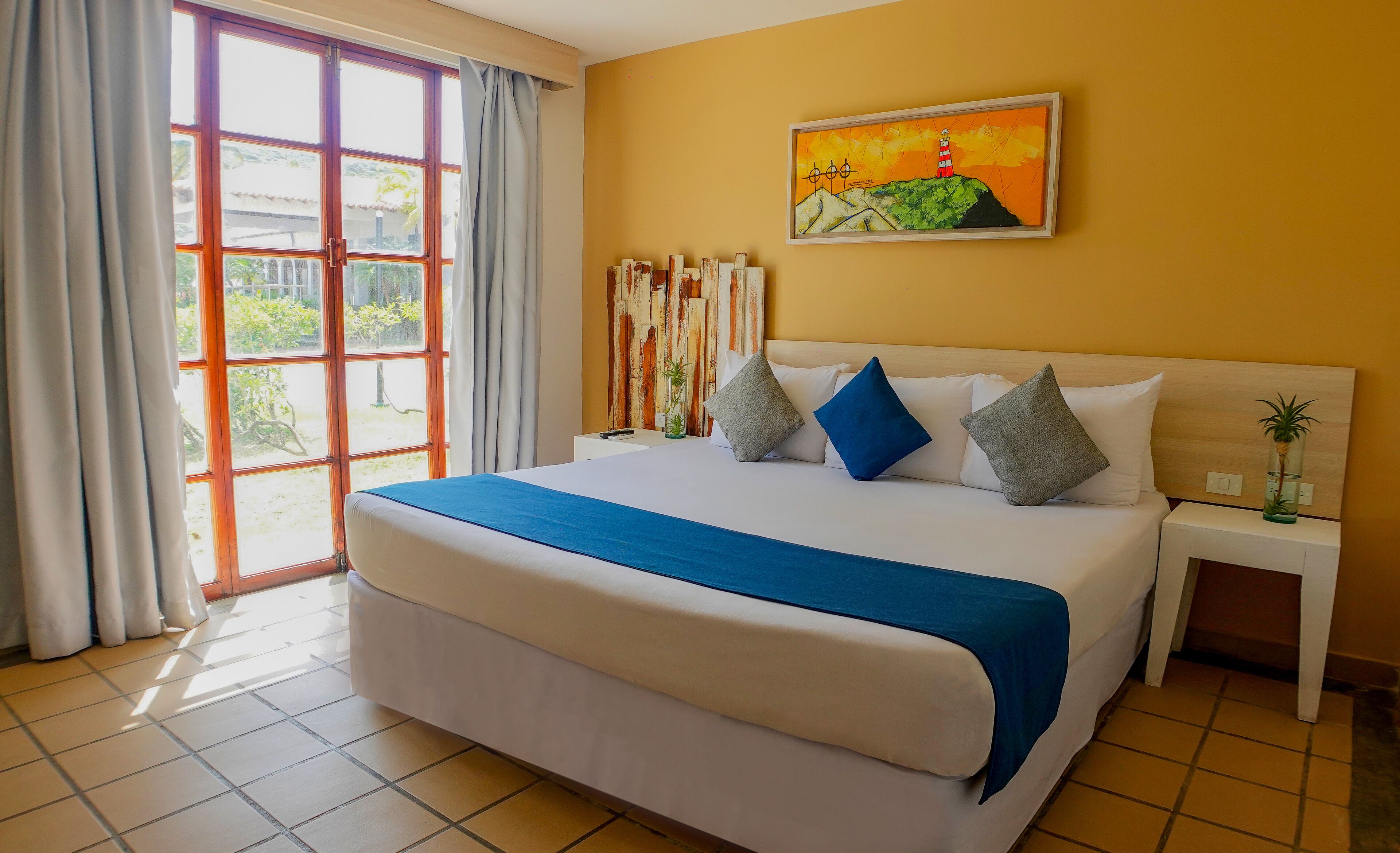 A hotel room with a large bed, a painting on the wall, and a view through the window.