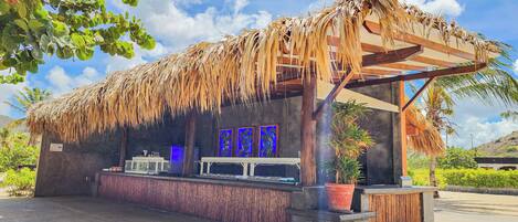 A thatched-roof structure with a wooden bench and a potted plant.