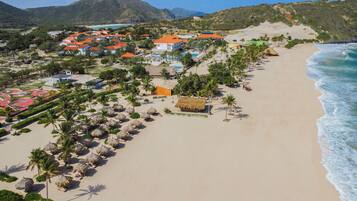 A coastal resort with beachside huts, palm trees, and a mountain backdrop.