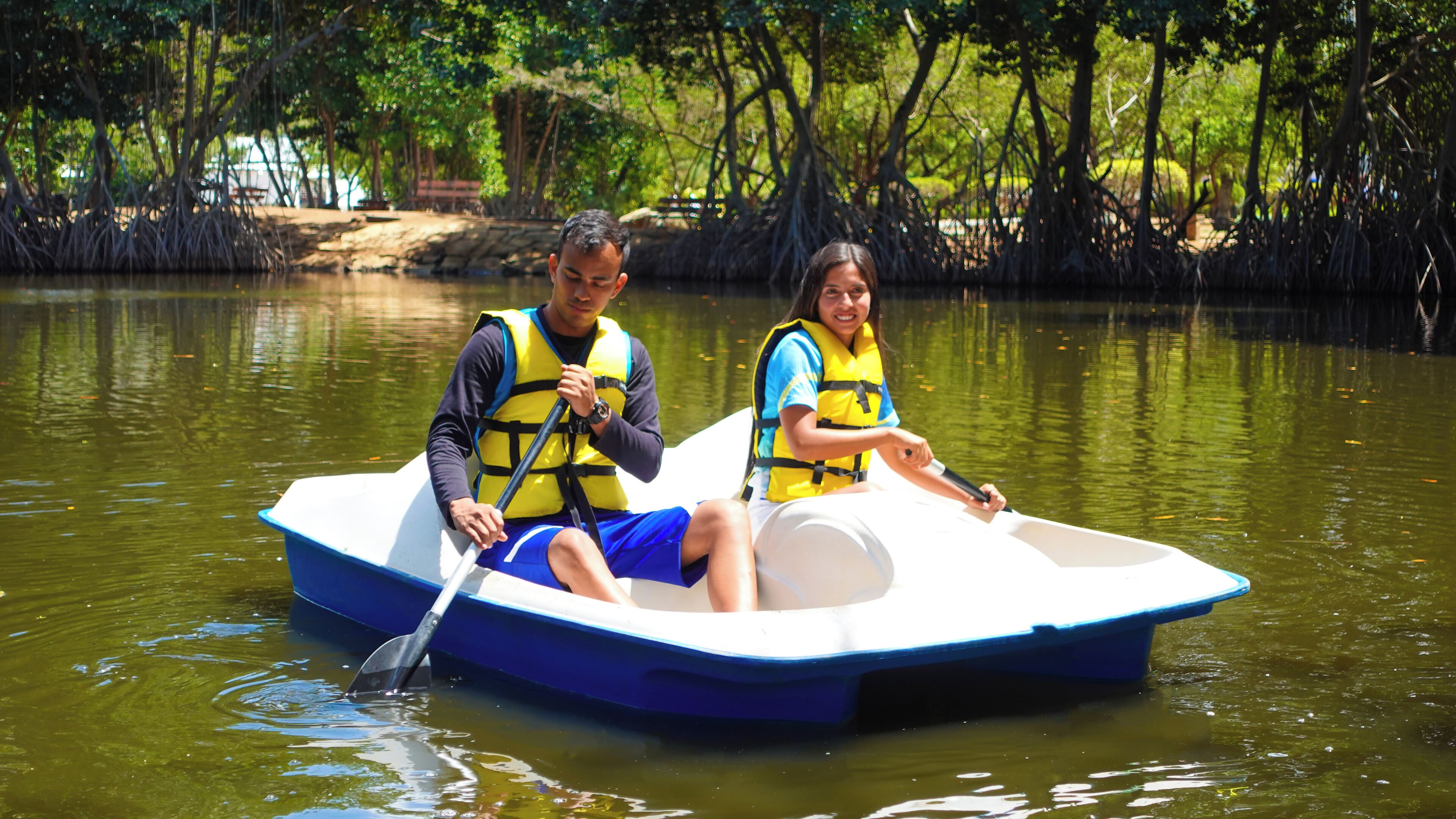 Two people in a small boat on a calm body of water surrounded by trees.