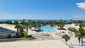 Uma área de piscina em resort, com vista para o oceano, cercada por palmeiras e espreguiçadeiras.
