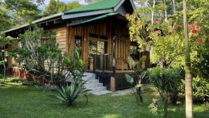 Een houten hut met een groen dak, omringd door weelderige begroeiing en een kleine trap naar de ingang.