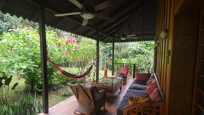 Een overdekt terras met een hangmat, rieten stoelen, een tafel met glazen blad en een bank.