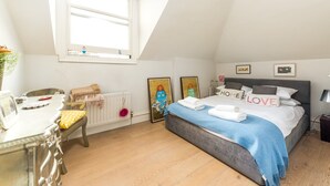 A bedroom with a bed, a desk, a chair, a radiator, and artwork on the walls. - Lofty Ideals (London)