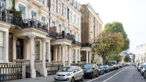 A row of traditional London townhouses with white facades, black iron railings, and a tree with yellow leaves in the foreground. - Lofty Ideals (London)