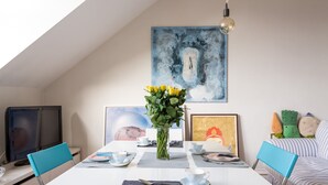 A dining area with a white table, blue chairs, a vase of yellow flowers, and artwork on the walls. - Lofty Ideals (London)
