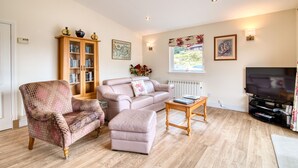 A living room with a sofa, armchair, ottoman, wooden cabinet, television, and a window with a view. - Kingfisher Lodge with sensational loch views (Crianlarich)