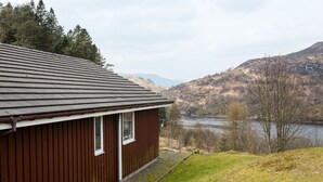 A brown wooden building with a sloped roof, located near a body of water and surrounded by hills. - Kingfisher Lodge with sensational loch views (Crianlarich)