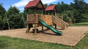A wooden playground with a slide and swings.