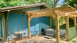 A wooden pergola structure with a table and chairs underneath, a barbecue grill, and a covered seating area.