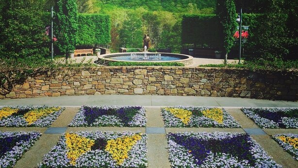 A landscaped garden with a fountain, stone wall, and flower beds.