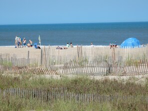 A beach with a wooden fence, people relaxing, and a blue umbrella.