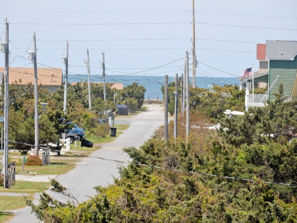A residential street with houses, power lines, and a clear view of the ocean.