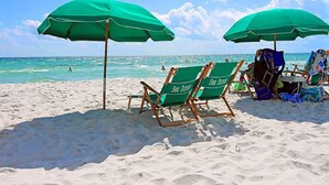Una playa con dos sombrillas verdes y dos sillas de playa identificadas como 'Sea Dunes'.