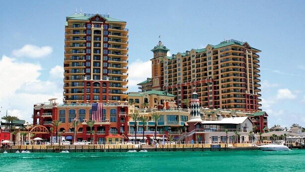 Un hotel frente al mar con varios edificios altos, un puerto deportivo y una destacada bandera estadounidense.