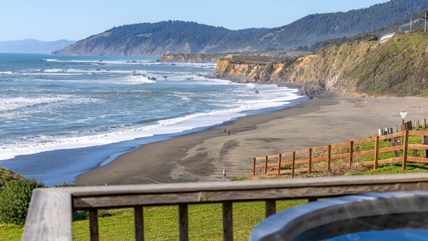 Una playa con valla de madera, terraza de madera y jacuzzi.